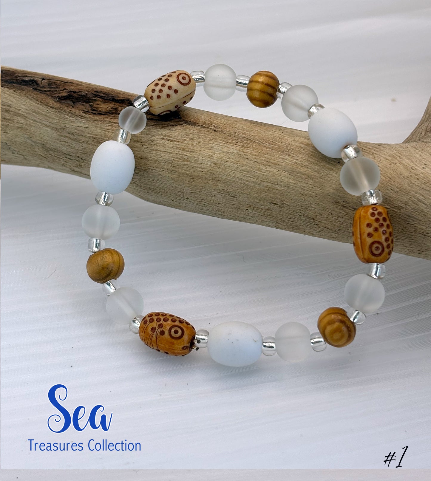 Beaded bracelet with white, brown, and clear beads on a wooden branch with 'Sea Treasures Collection' branding.