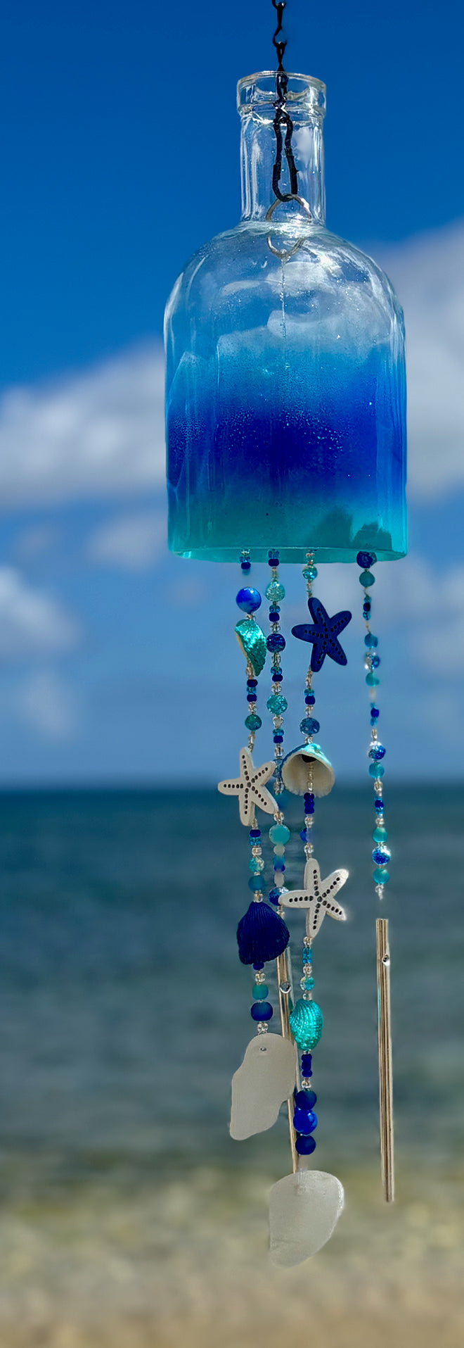 Decorative bottle wind chime with beach-themed beads against a blurred ocean background