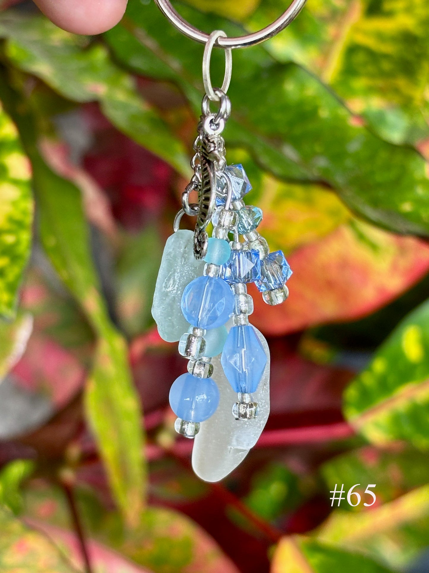 Keychain with blue beads and a leaf against a colorful plant background