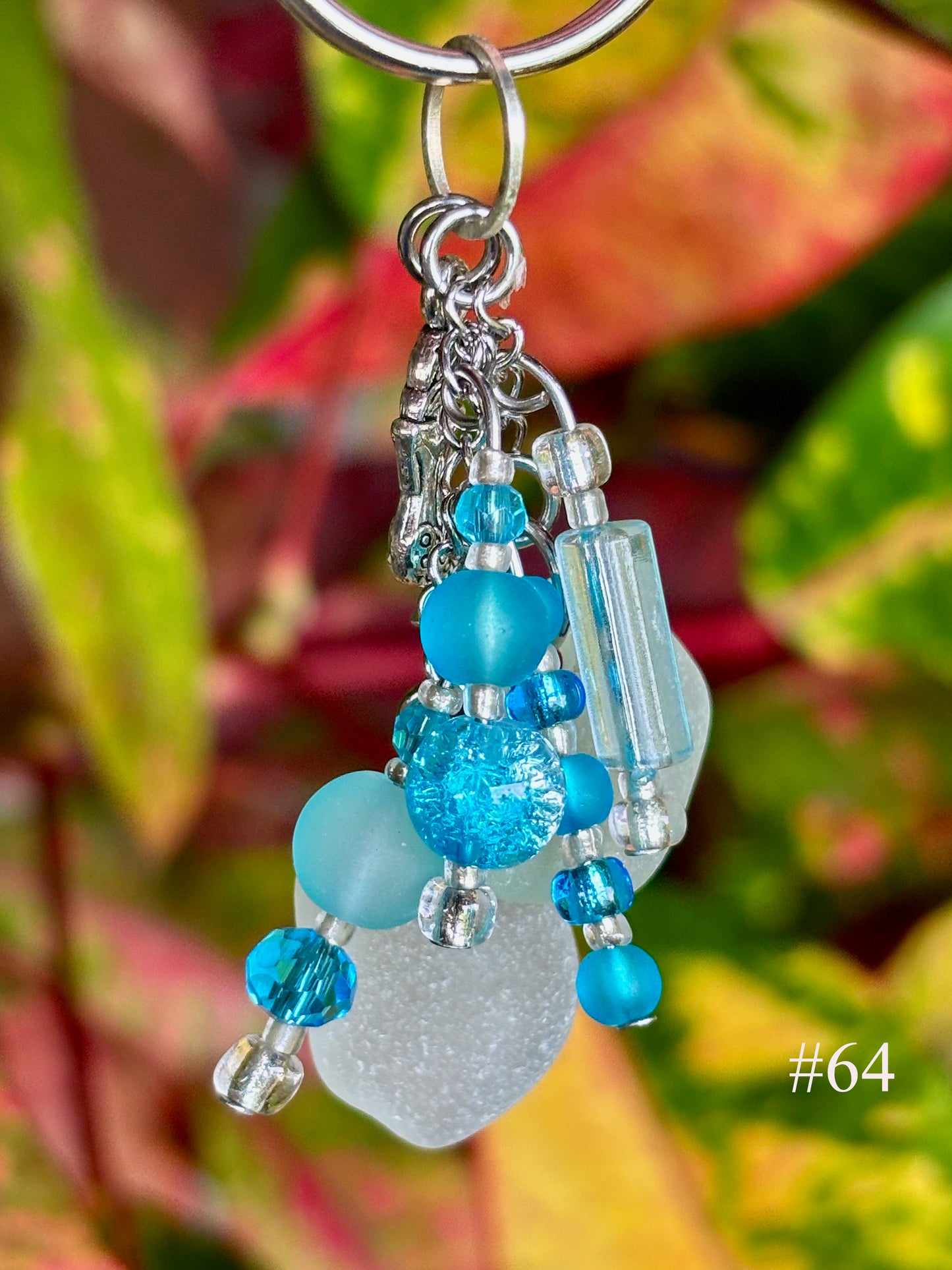 Beaded keychain with blue and clear beads against a blurred green and red leaf background
