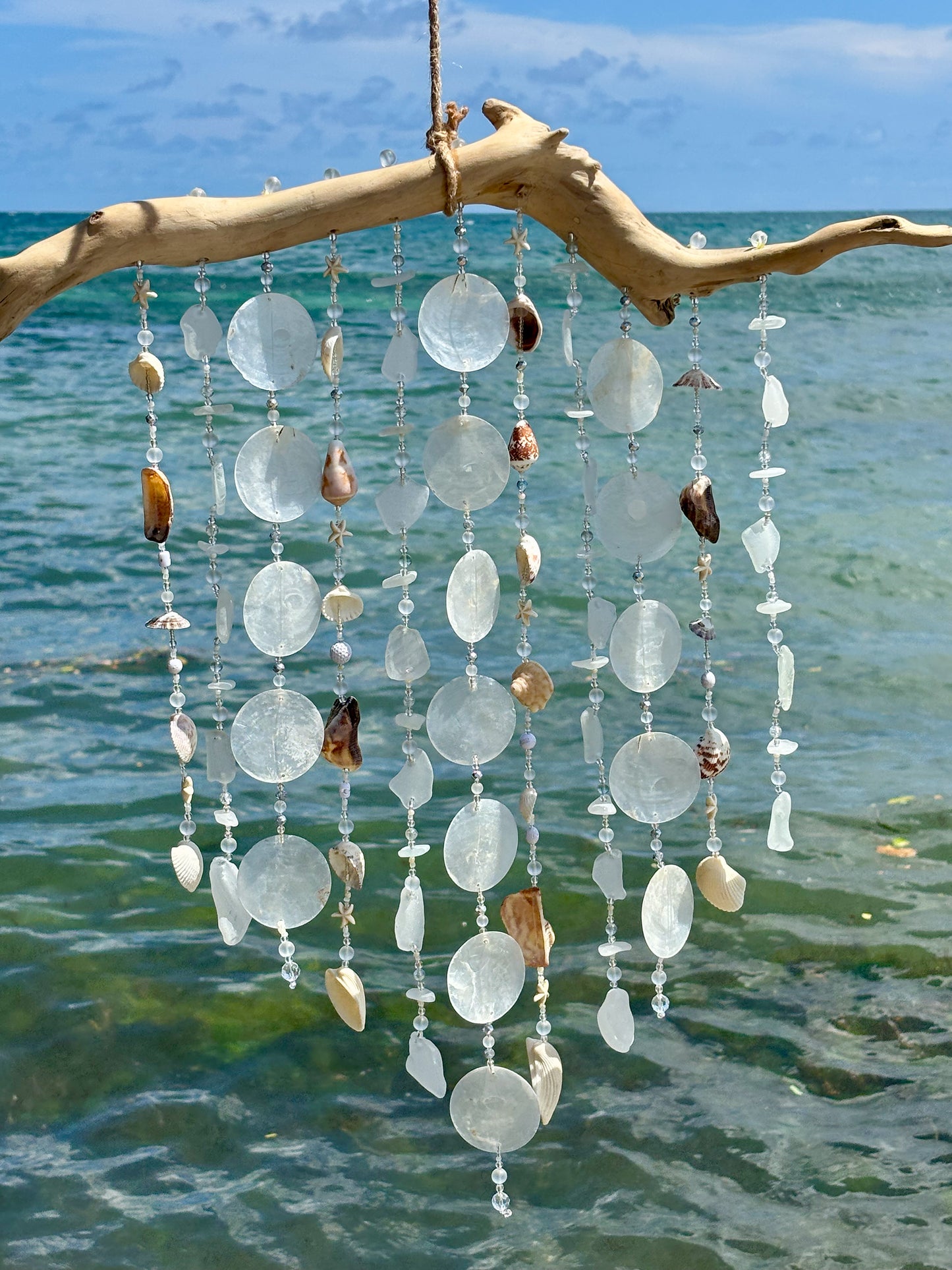 Decorative hanging mobile with seashells and beads against a beach background