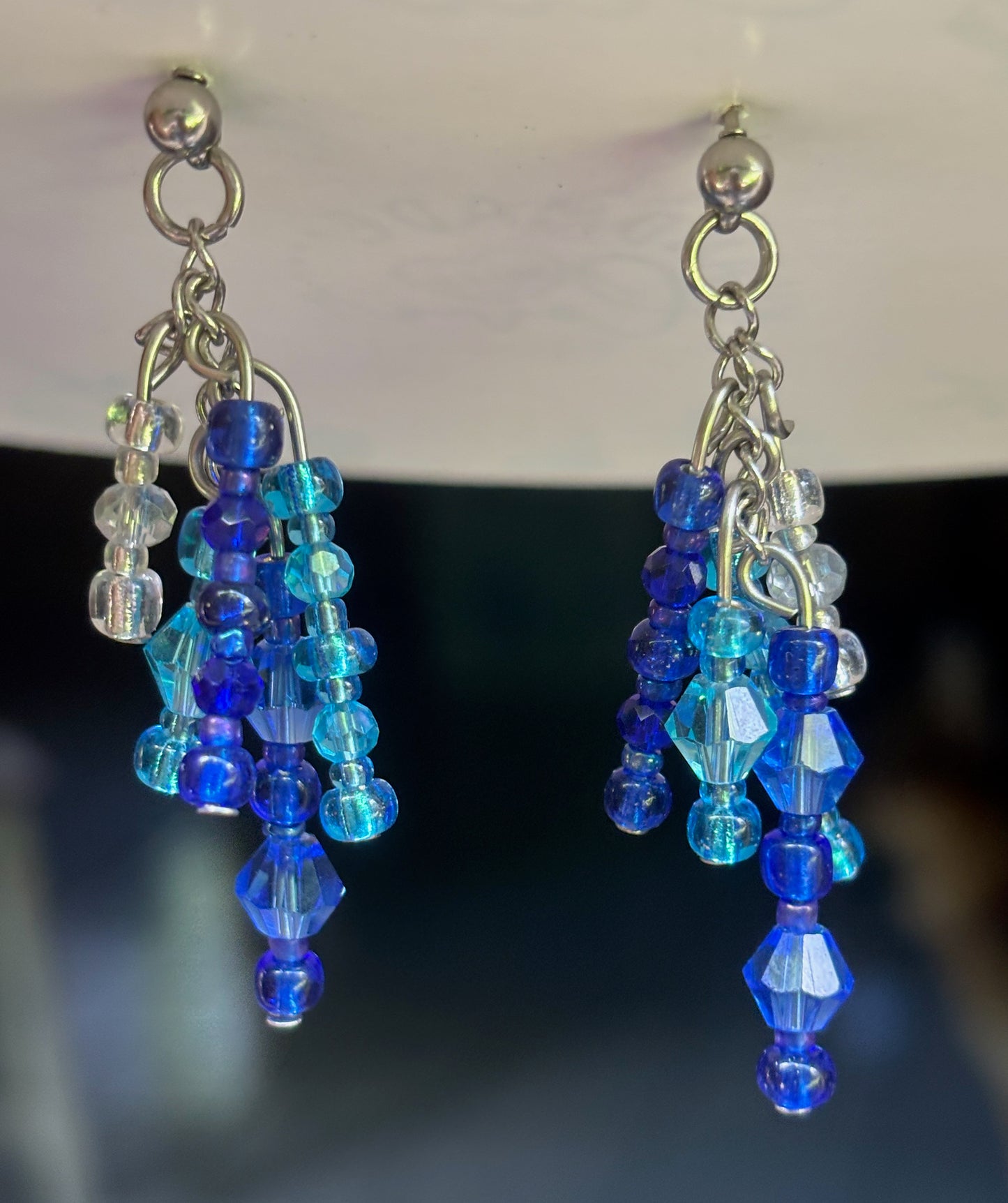 Blue beaded earrings with silver hooks on a dark background