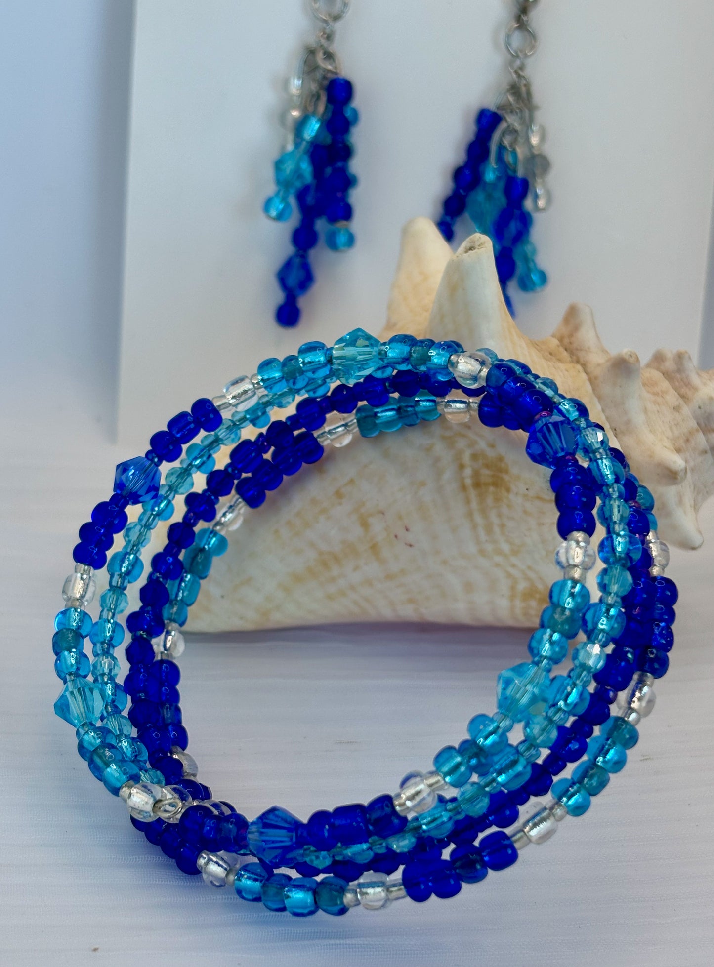 Blue beaded bracelet and earrings on a white background with shells.