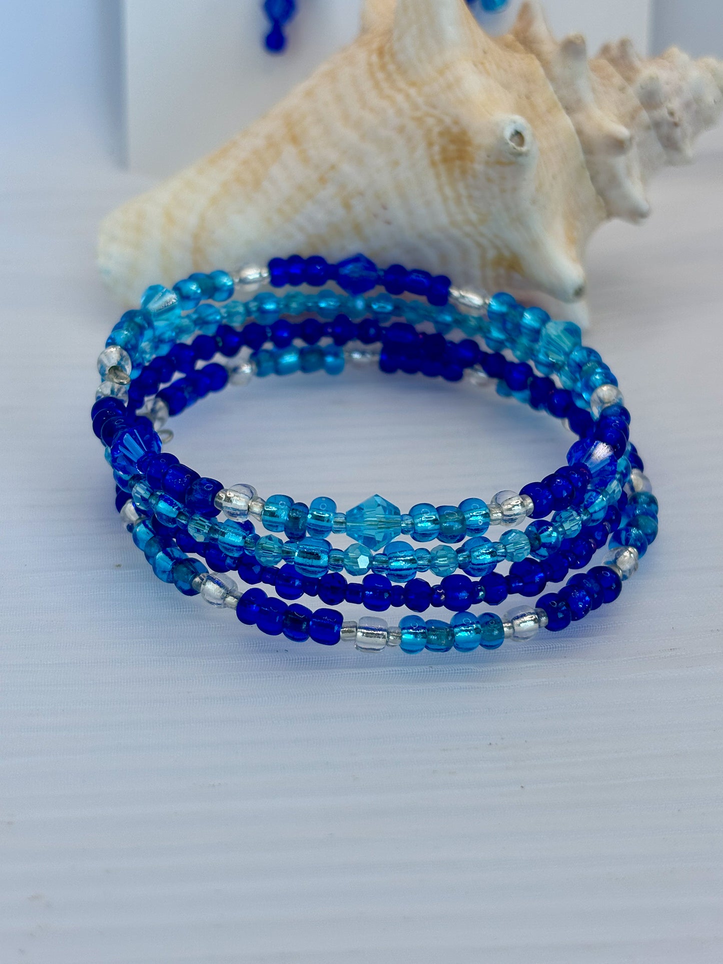 Set of blue beaded bracelets on a white surface with seashells in the background