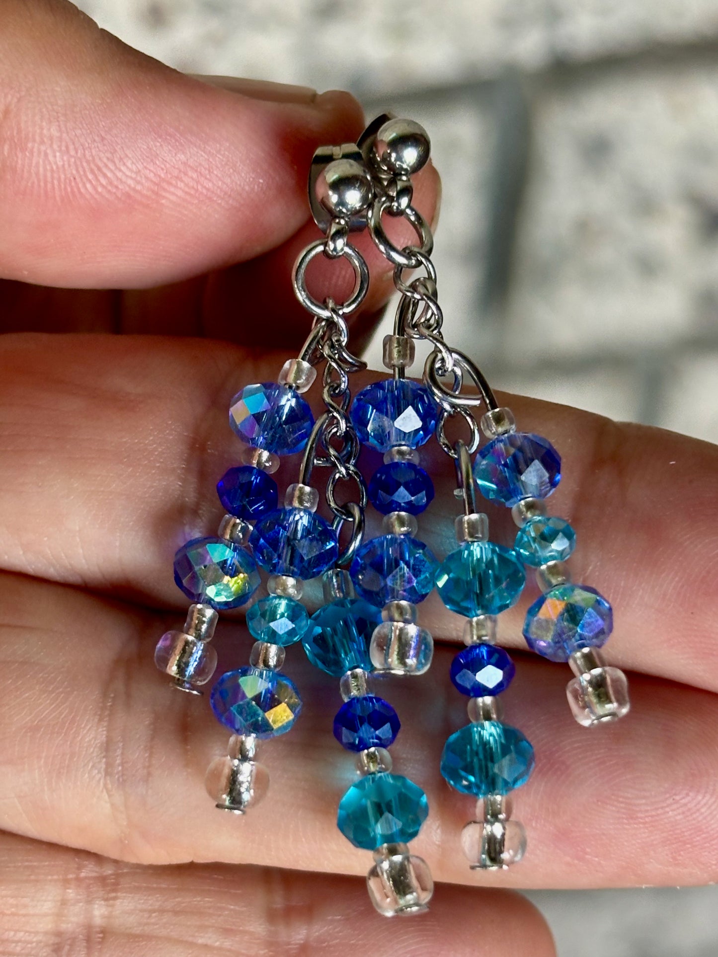 Blue beaded earrings held between fingers with a blurred background