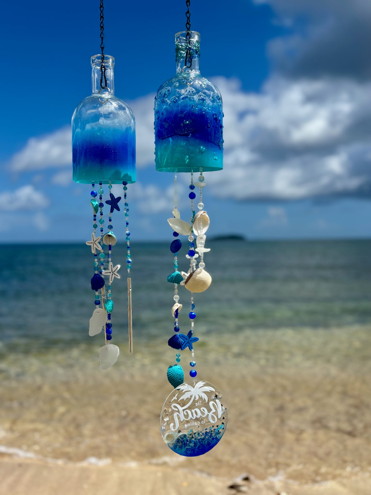 Decorative bottle wind chimes with blue and clear design against a beach backdrop