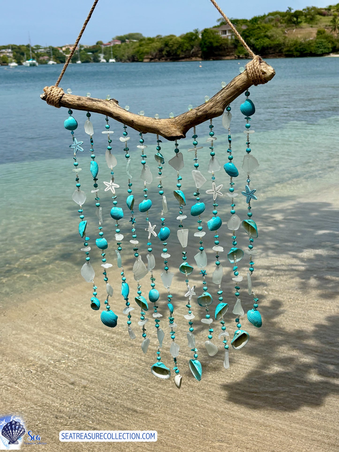 Decorative wind chime with turquoise beads and seashells hanging on a beach.