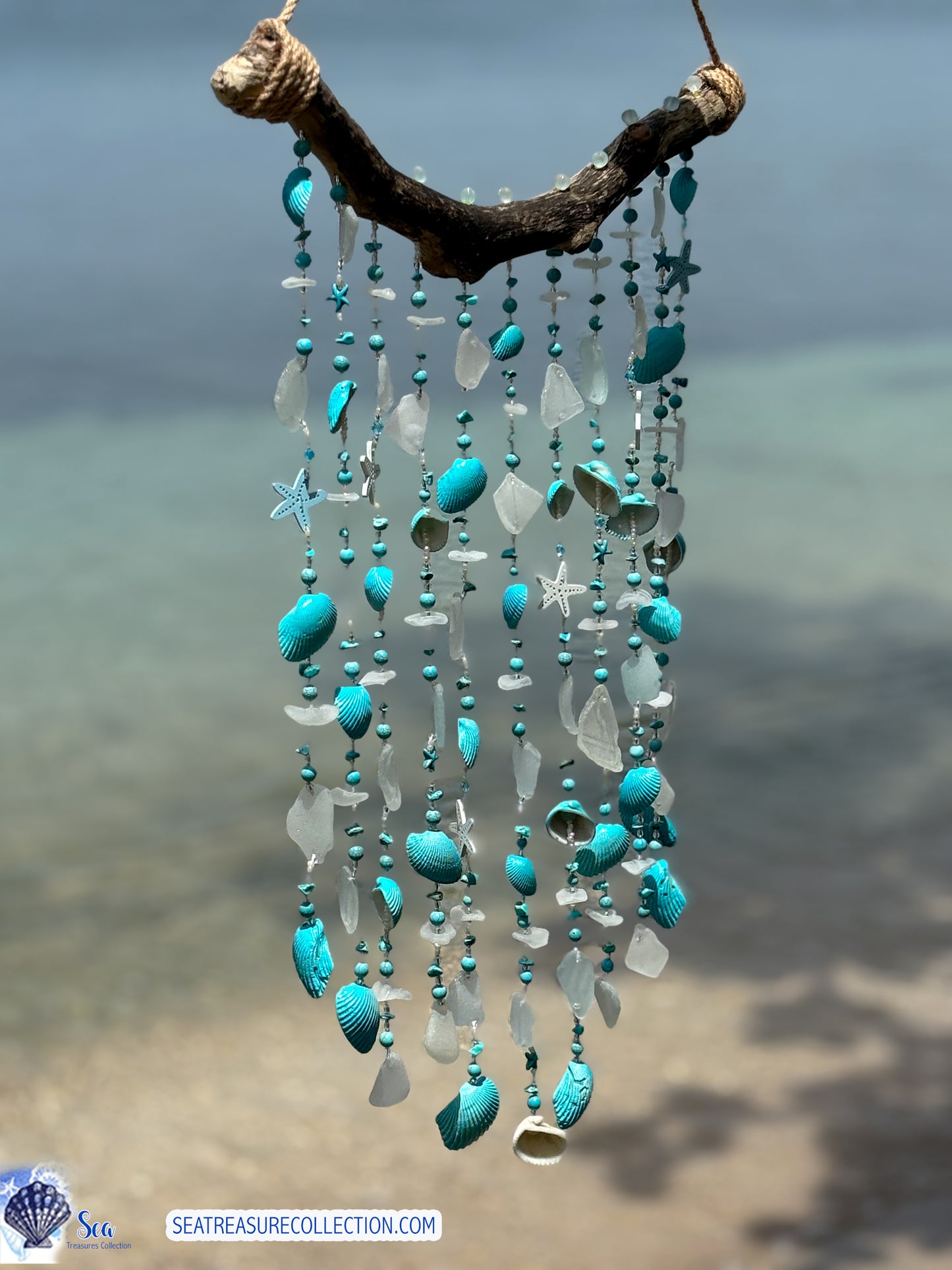 Decorative wind chime with turquoise and white beads and shells against a blurred beach background.