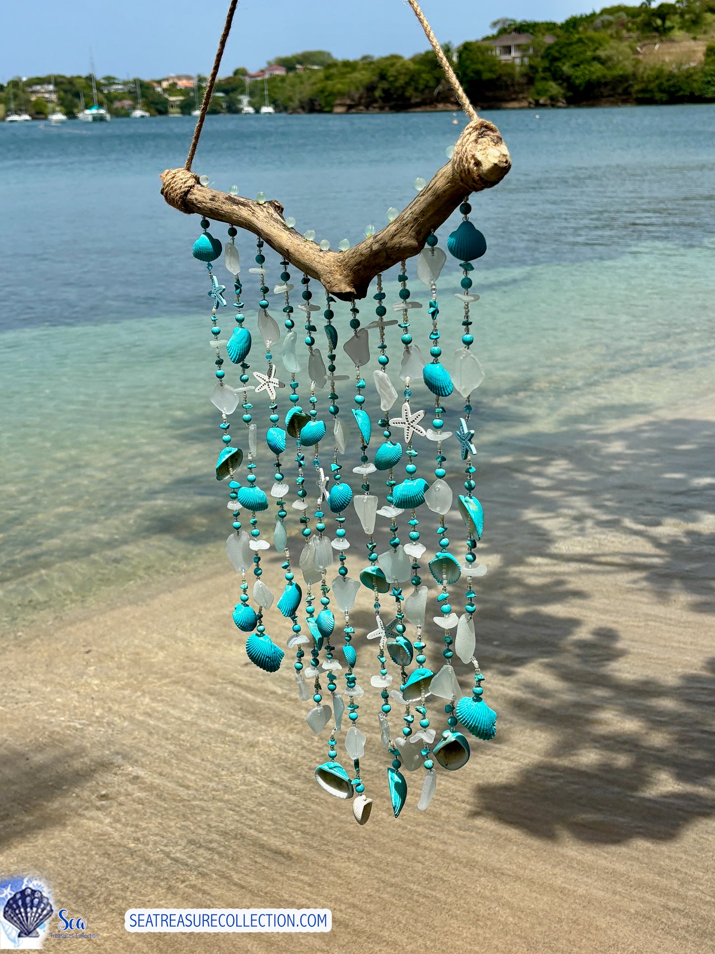 Decorative wind chime with turquoise beads and shells hanging on a beach.