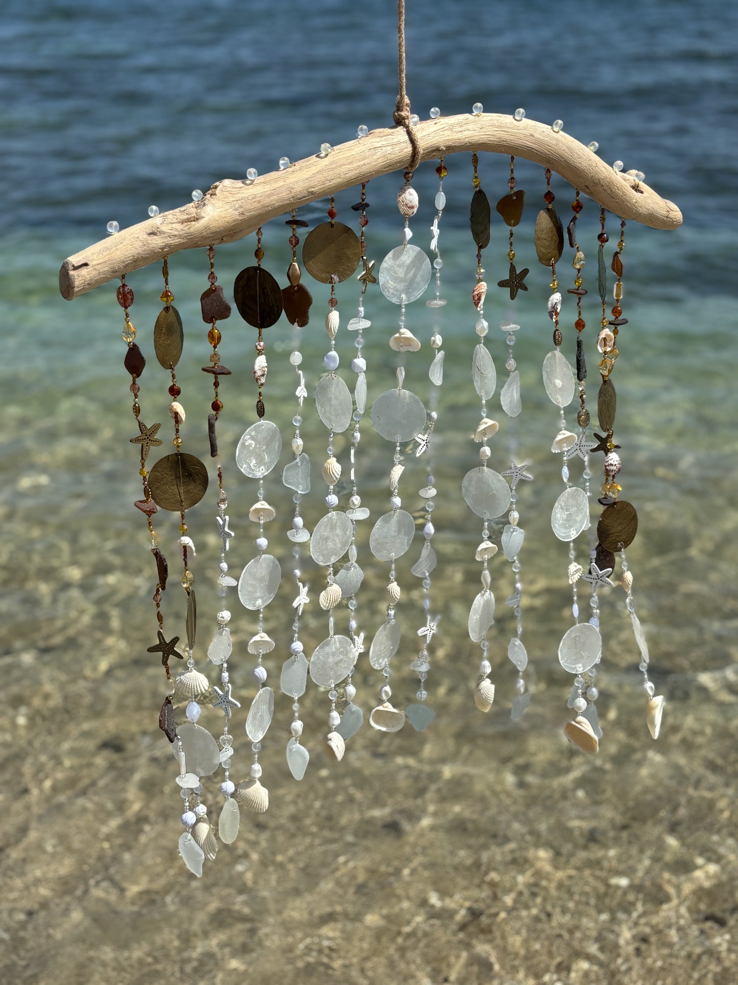 Decorative wind chime with natural elements hanging by a body of water