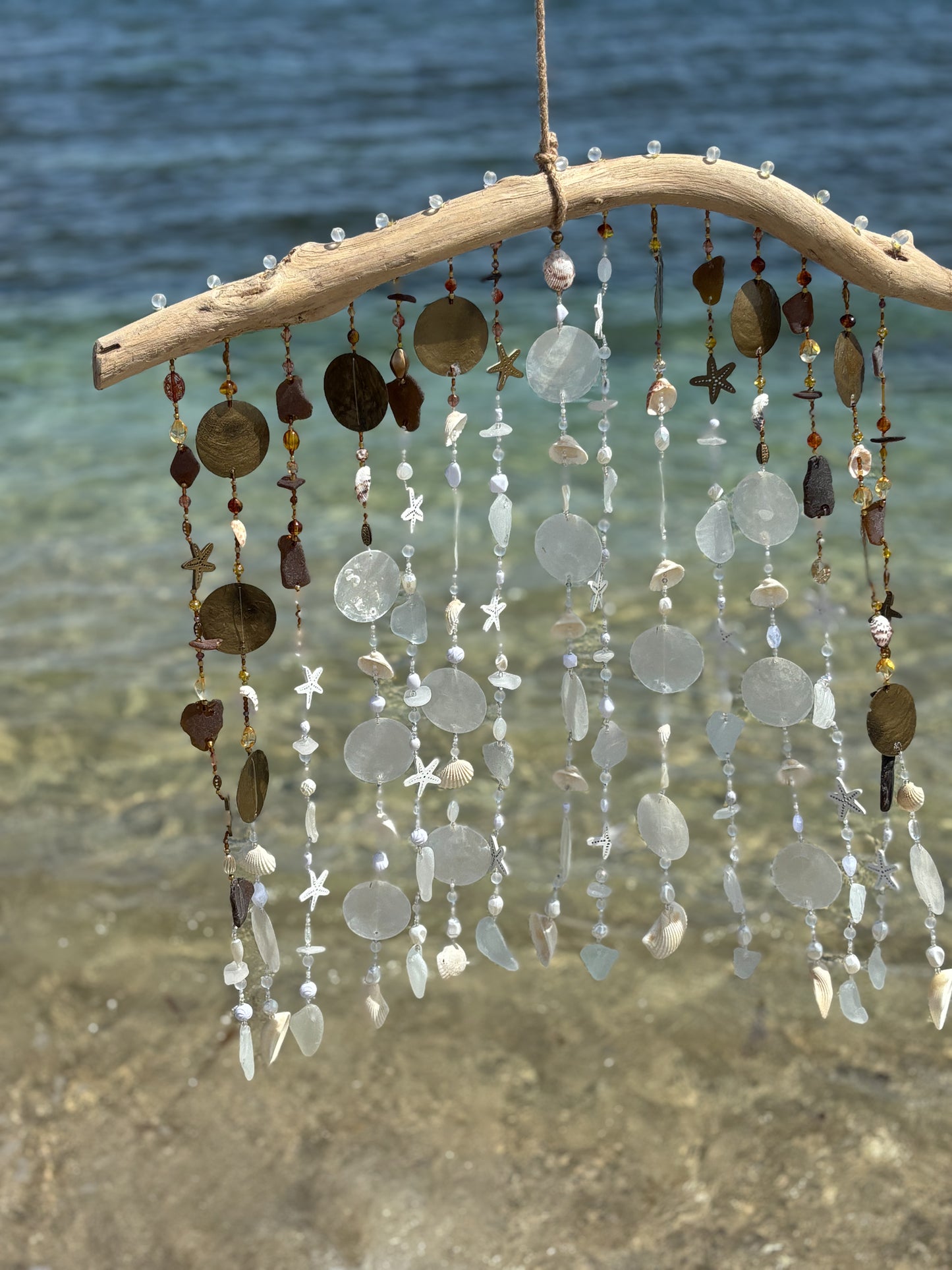 Decorative hanging mobile with shells, sea glass and beads by a body of water