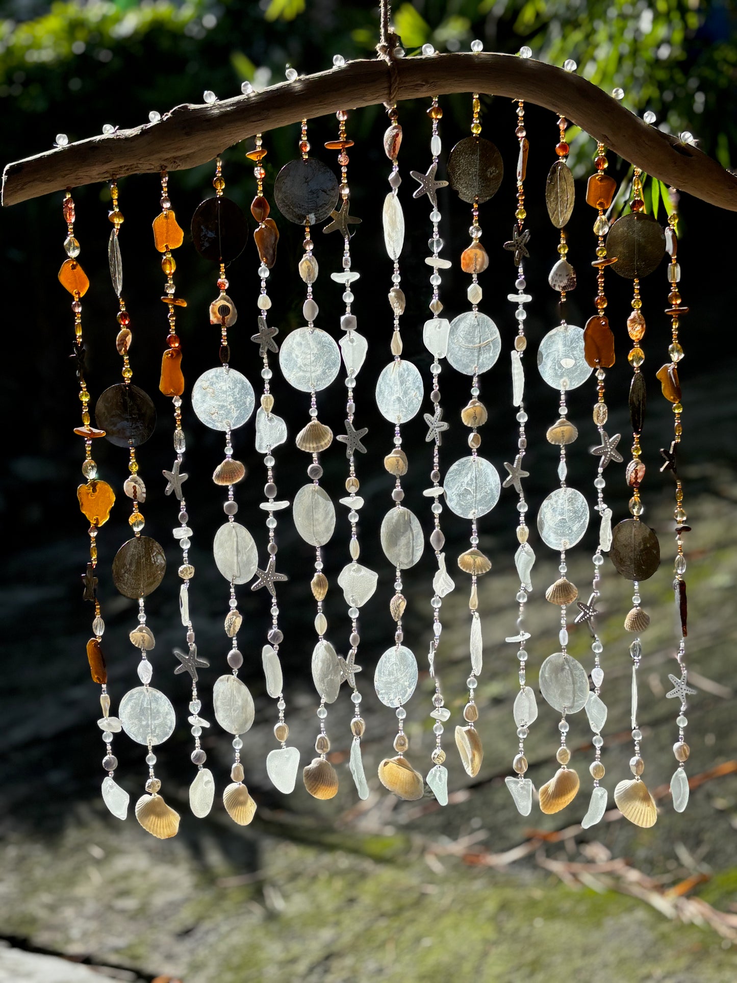 Decorative white, brown sea glass wind chime with beads and shells on a natural background
