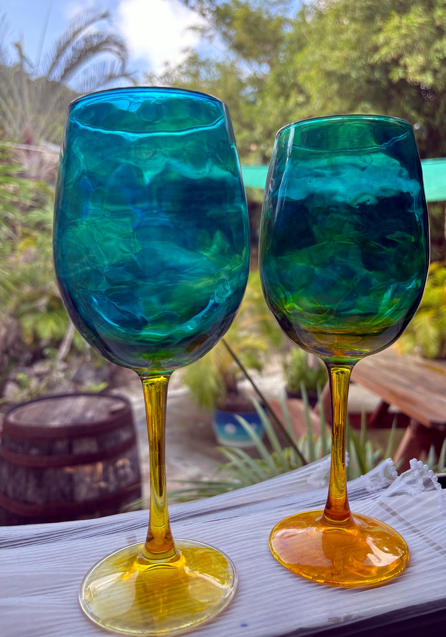 Two blue and green glass goblets on a table with a blurred outdoor background