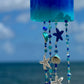 Decorative bottle wind chime with beach-themed beads against a blurred ocean background