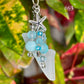 Decorative keychain with blue beads, starfish charm, and white leaf-shaped pendant on a green leaf background.
