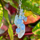 Keychain with blue beads and a leaf against a colorful plant background