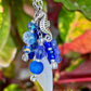 Decorative keychain with blue beads, a seashell, and a seahorse charm against a leafy background.