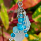 Beaded keychain with blue and clear beads against a blurred green and red leaf background