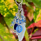Decorative keychain with blue and silver charms against a leafy background