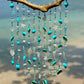 Decorative sea glass and sea shell wind chime with turquoise beads and shells against a blurred beach background
