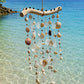 Front view of a handcrafted driftwood wind chime with natural seashells and glass accents.