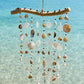Handcrafted Seashell Serenity Driftwood Wind Chime made in Grenada hanging over clear Caribbean water.