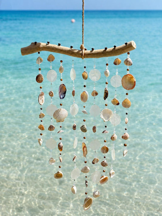 Handcrafted Seashell Serenity Driftwood Wind Chime made in Grenada hanging over clear Caribbean water.