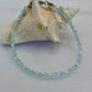 Turquoise beaded anklet on a white surface with a large shell in the background