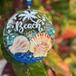 Decorative beach-themed suncatcher with shells and 'Beach' text on a blurred natural background.