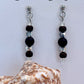 Black and shiny beaded earrings with a shell on a light gray background
