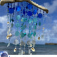 Decorative beach sea glass wind chime with blue and white beads and shells against a beach background.