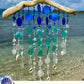 Decorative wind chime with blue and white sea glass, beads and seashells against a beach background.