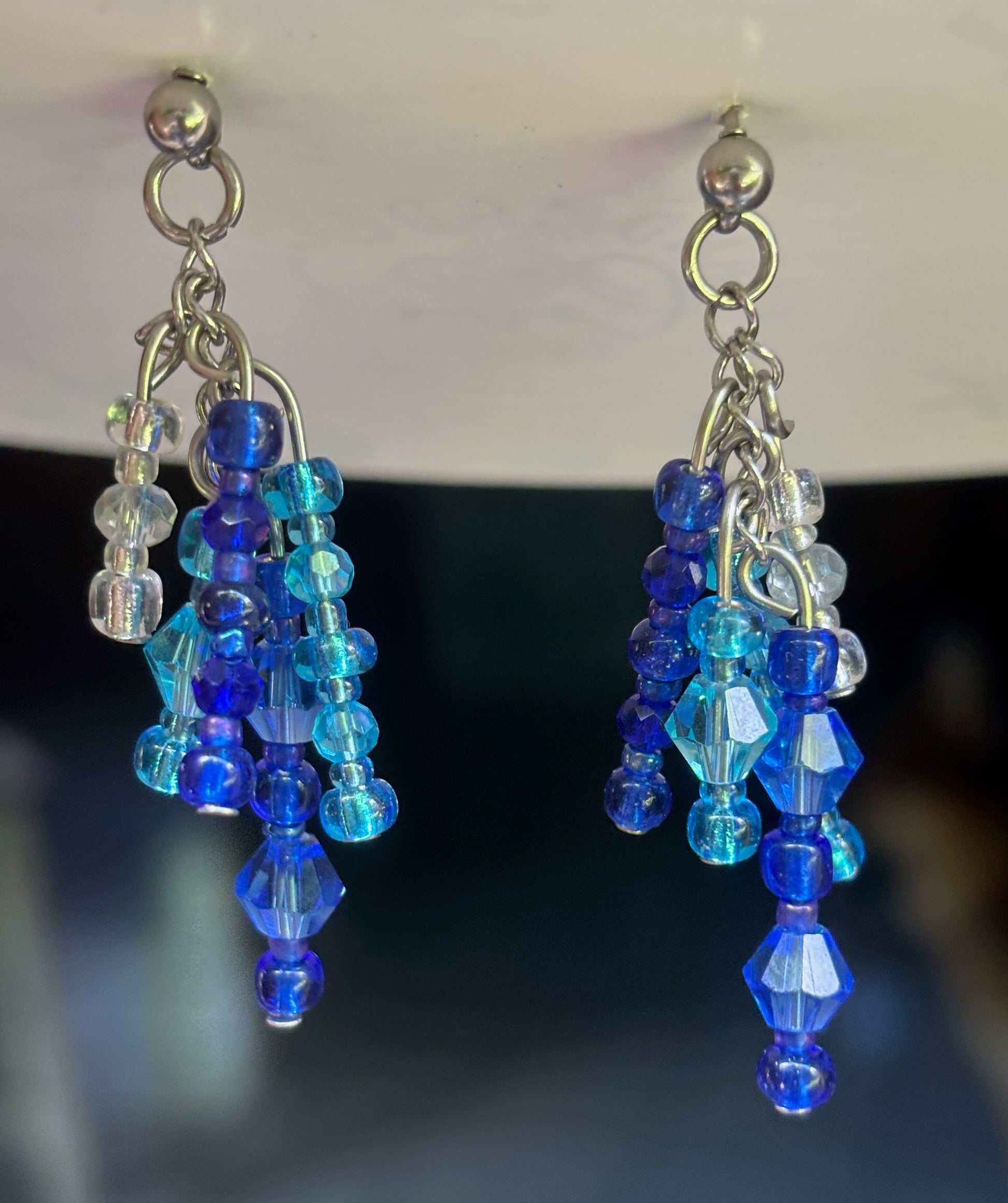 Blue beaded earrings with silver hooks on a dark background
