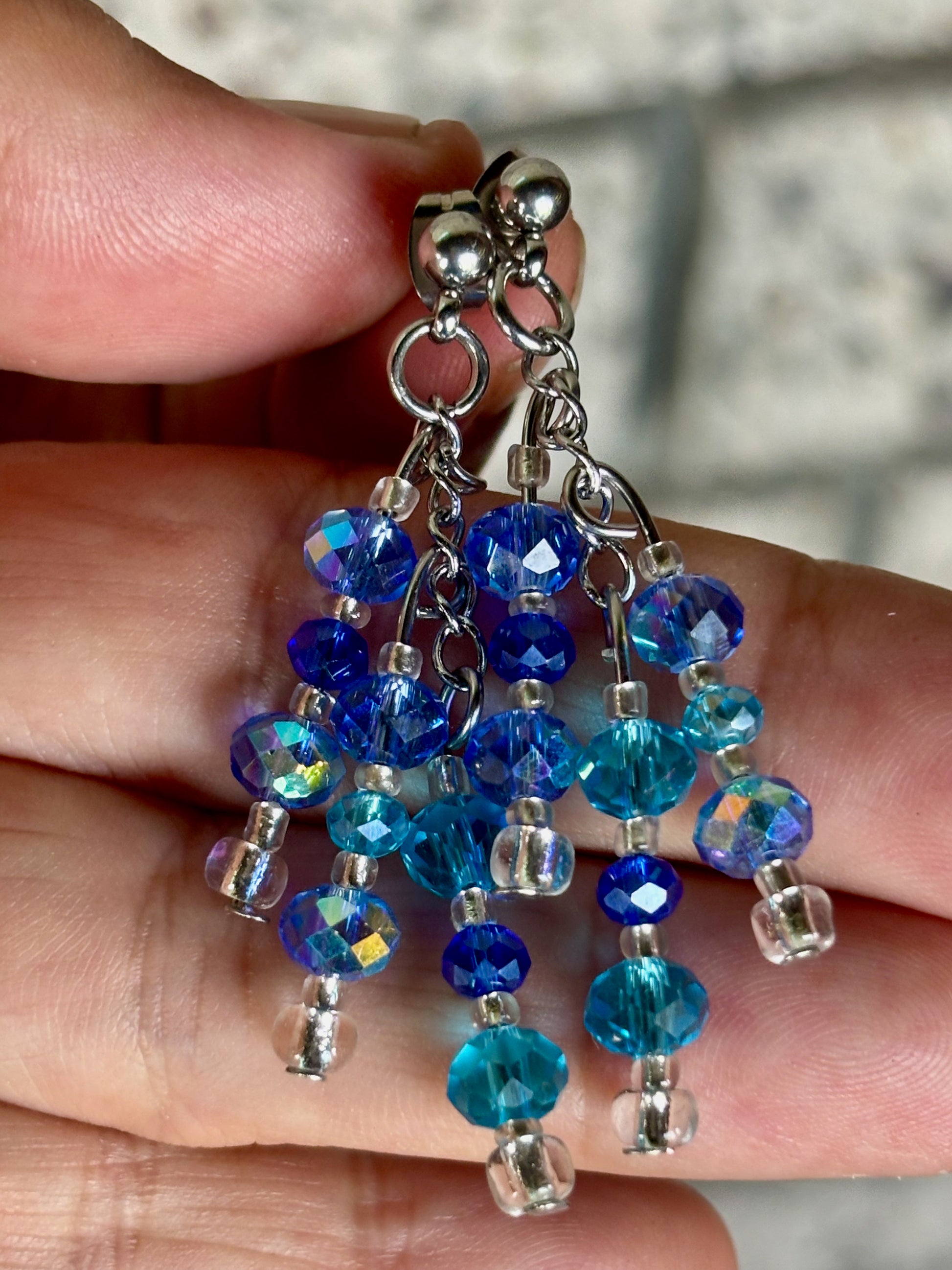 Blue beaded earrings held between fingers with a blurred background