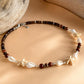 A beaded bracelet with dark brown wooden beads, white seashells, and starfish charms, displayed on a beige background with driftwood props.