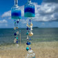 Decorative bottle wind chimes with blue and clear design against a beach backdrop