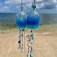 Two rum bottle wind chimes with decorative elements hanging against a beach background.