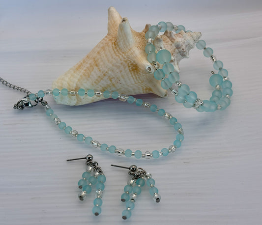 Turquoise beaded anklet, bracelet and earrings with a shell on a light background