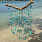 Decorative wind chime with turquoise beads and seashells hanging on a beach.
