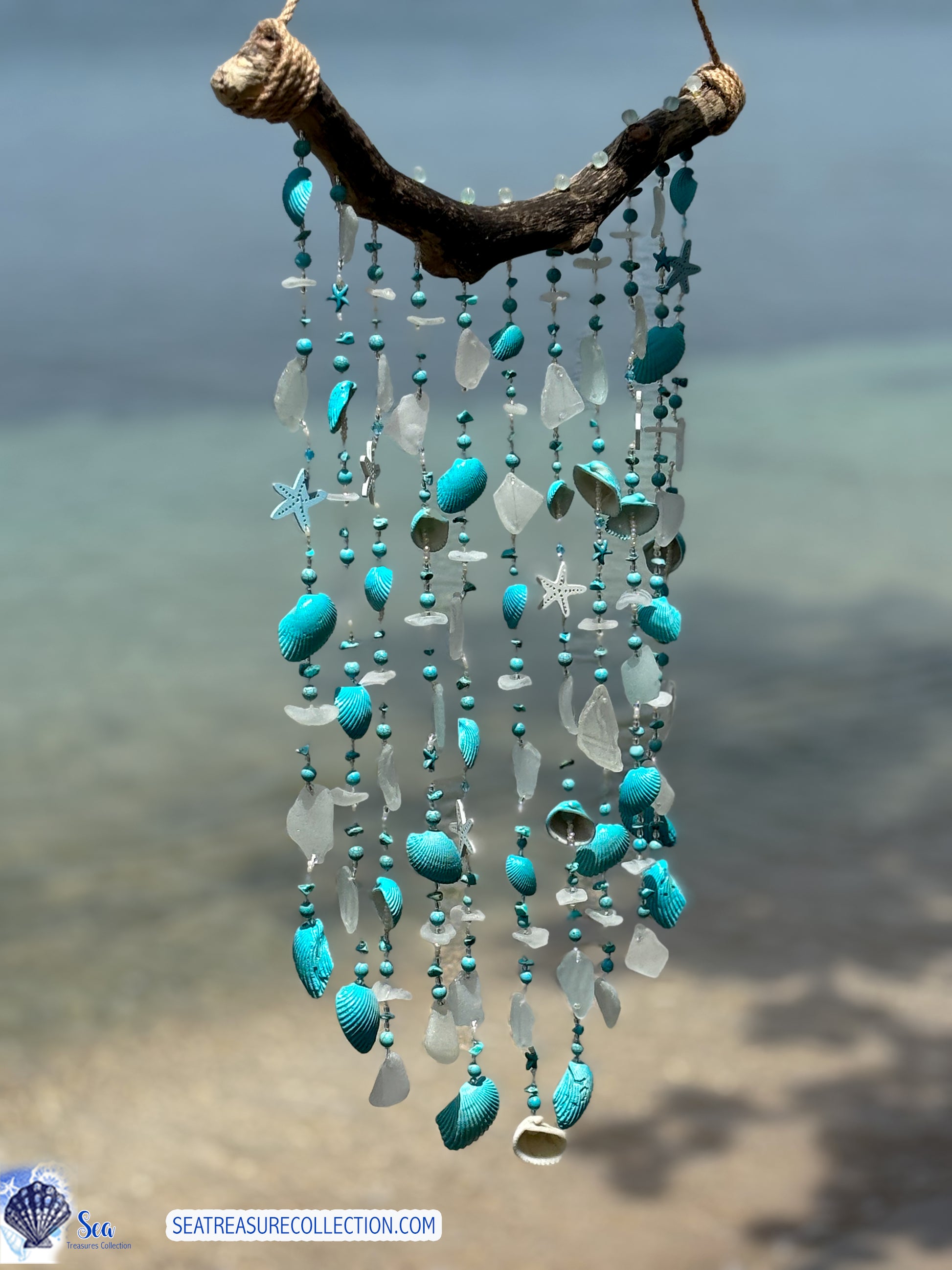 Decorative wind chime with turquoise and white beads and shells against a blurred beach background.