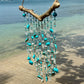 Decorative wind chime with turquoise beads and shells hanging on a beach.