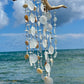 Decorative shell and driftwood wind chime against a blue sky and ocean background