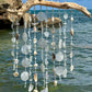 Decorative wind chime with seashells and beads hanging by a body of water.