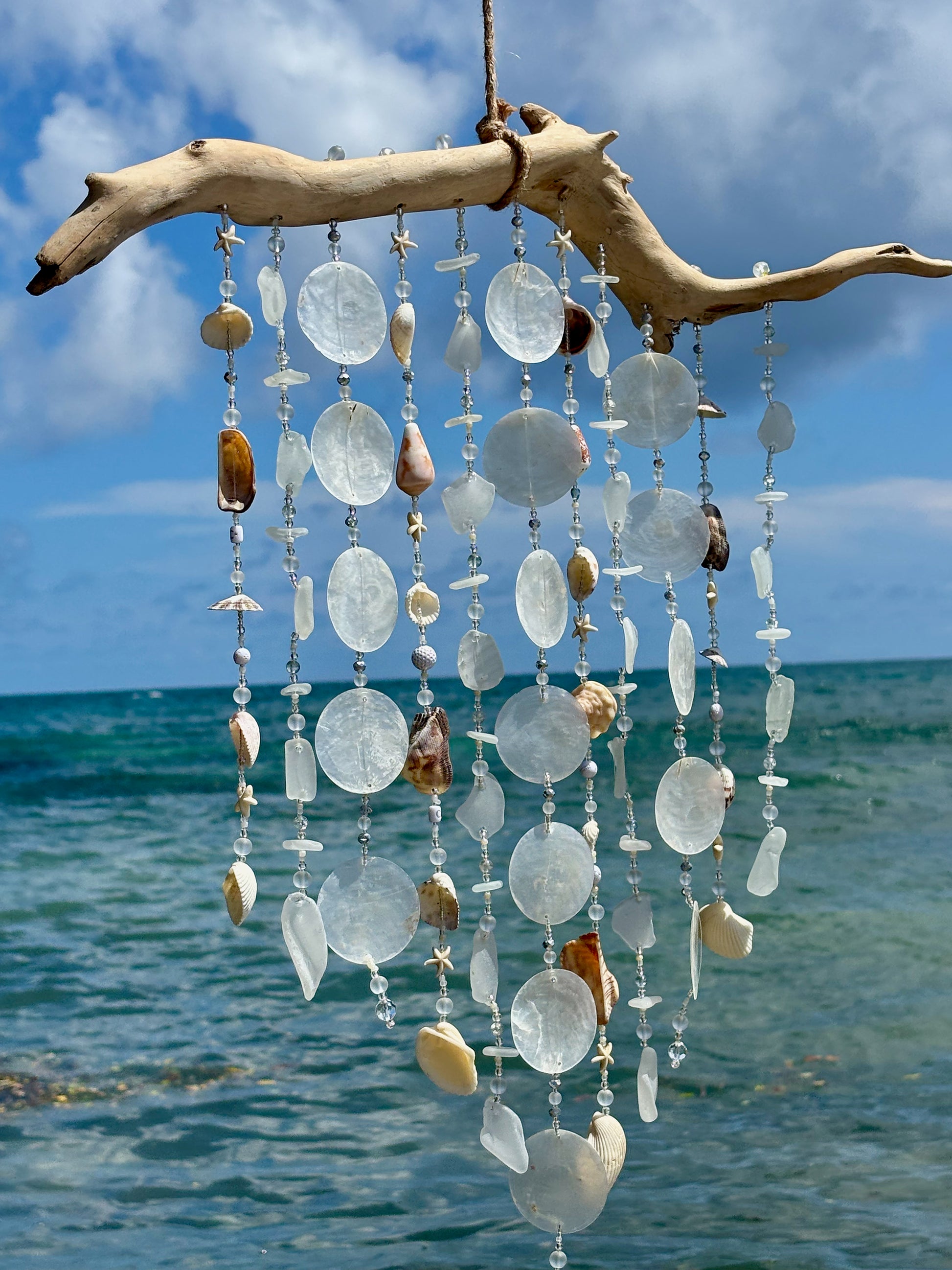 Decorative wind chime with natural elements against a blue sky and ocean background