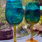 Two blue and green glass goblets on a table with a blurred outdoor background